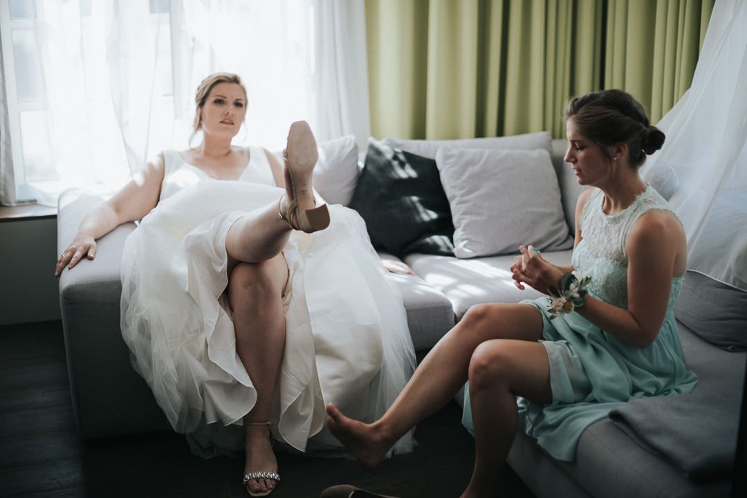 Hochzeit-im-Heyligenstaedt Braut sitzt mit ihrer Trauzeugin auf der Couch und begutachtet ihrer Schuhe.