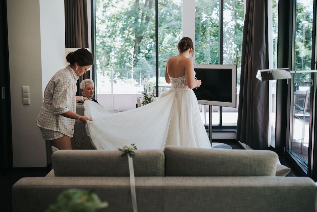 Hochzeit-Burg-Schwarzenstein-Getting-Ready.jpg Trauzeugin breitet das Brautkleid aus.