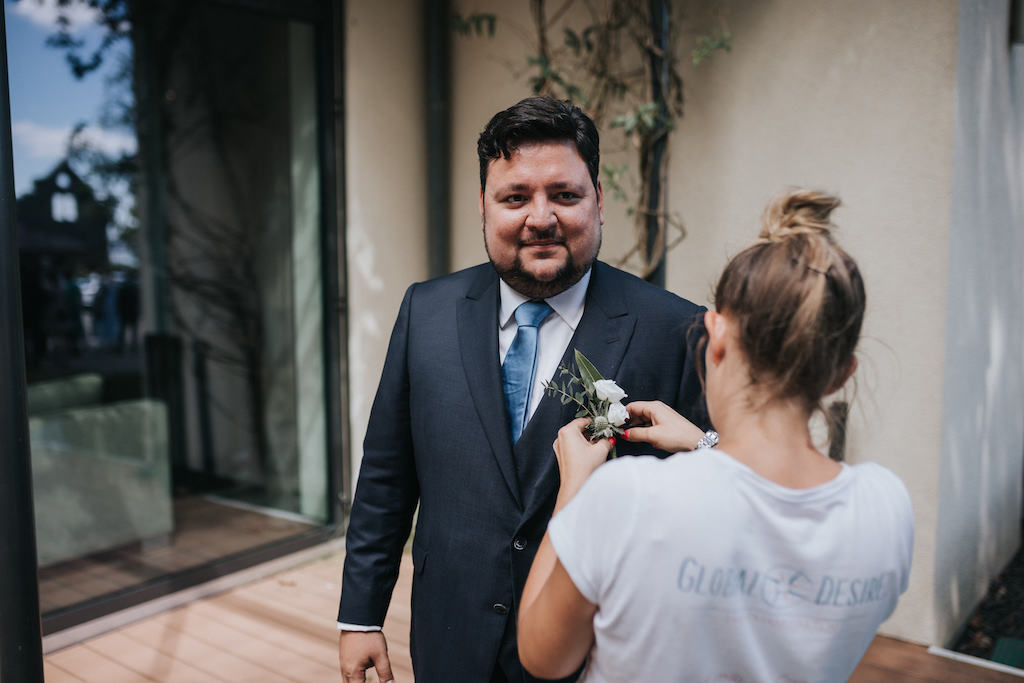 Hochzeit-auf-Burg-Schwarzenstein-Getting-Ready.jpg Ansteckblume wird am Anzug des Bräutigams angebracht.